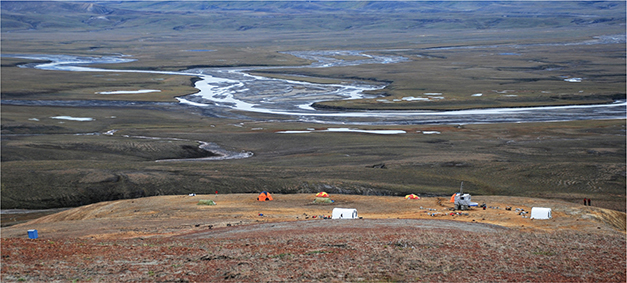 Fig. 2 The Rødryggen-1 drill-site and camp, viewed approximately towards the west with the broad plain of Storsletten as backdrop (Photo: Annette Ryge). The rig was placed on the brightly coloured, yellow-weathering mudstones of the Albrechts Bugt Member (Palnatokes Bjerg Formation). The overlying Rødryggen Member (Palnatokes Bjerg Formation) in the foreground consists of purple to brick-red mudstones. Debris from this unit imparts the slopes of the landscape with a reddish colour that can be seen from afar, and from which is derived the location’s name Rødryggen, meaning “the red ridge.”