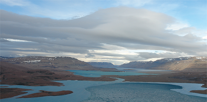 Fig. 4 Slusen [the sluice], the short river linking the two lakes, Øvre Midsommersø in the distance and Nedre Midsommersø in the foreground (viewed towards the west). The Portfjeld Group is particularly well-exposed in the steep cliffs on both sides of Øvre Midsommersø.