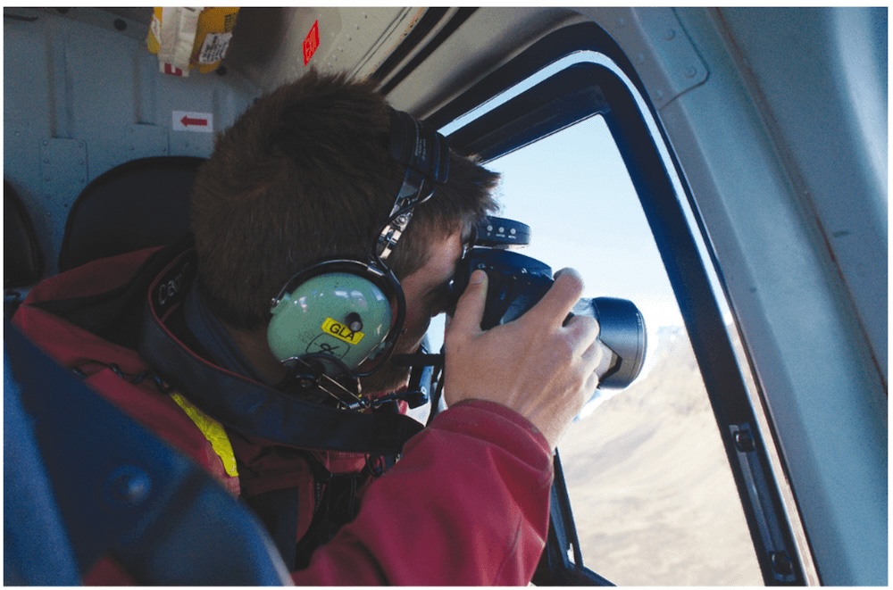 Man looks through window in helicopter holding a camera