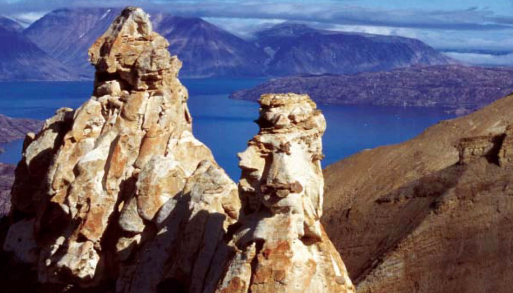 Pillars of rock with fjord and mountains in the background.